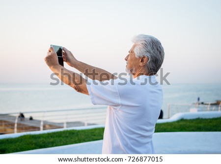 Middle -aged man taking photo of sunrise at sea