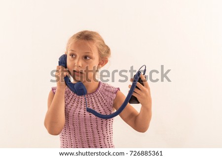 A girl in a pink knitted dress plays with an old telephone and very emotionally talks. White isolated background in studio. The concept of children and devices.