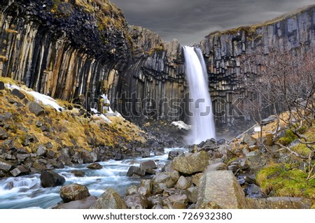 Long exposure picture of Svartifoss waterfall in Skaftafell national park in Iceland. Famous icelandic waterfall with dark dramatic stormy clouds. Black rock and white water. Iceland country side.
