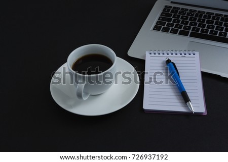 Close-up of black coffee, pen, notepad and laptop on black background