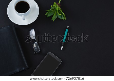 Overhead of black coffee, flora, pen, spectacles, mobile phone and organizer on black background