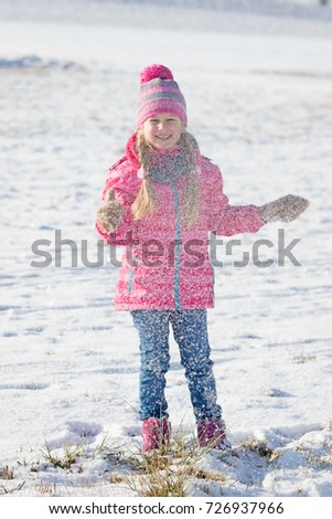 Young girl in warm hat playing with snow enjoying winter time