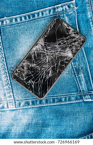 Broken glass screen of mobile phone on a jeans blue background