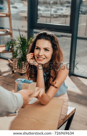partial view of man presenting gift to smiling girlfriend during date in cafe