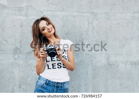 Stylish woman photographer in white with retro camera on the gray wall background. Image with copy space
