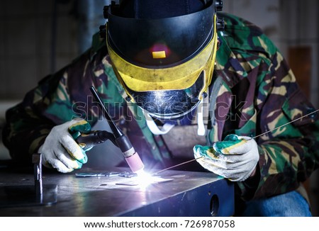 Professional welder working with steel material in workshop.Electric welding machine weld iron with hot electrode wire.Worker protective mask work on factory.Welding torch weld metal construction  Royalty-Free Stock Photo #726987058