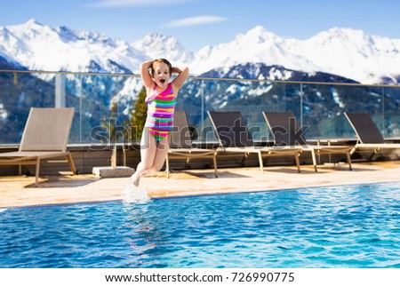 Little child playing in outdoor swimming pool of luxury alpine resort in the Alps mountains, Austria. Winter and snow vacation with kids. Hot tub outdoors with mountain view. Children play and swim.