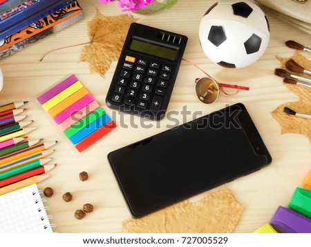 Stationery supplies and a smart phone with an empty screen on a wooden table