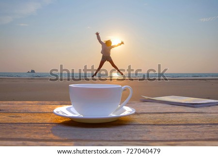 a selective focus picture of a cup of coffee on wooden table in the morning sunrise at public beach in the South of Thailand