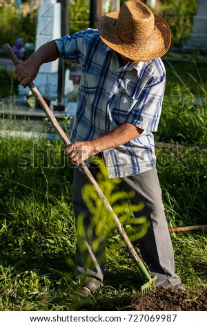 An elderly rural man in a straw hat is working near the grave in the cemetery.