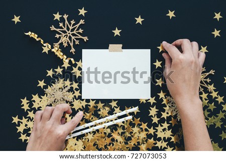 Christmas planning concept mock up. Note on black background with washi tape, gold stars confetti, serpentine and glitter snowflakes. Place for text flat lay