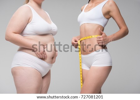 Thin girl measuring her abdomen near fat one Royalty-Free Stock Photo #727081201