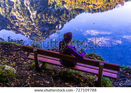Woman siting on a bench with the mountain reflecting in the water