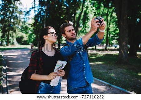 Couple in love making photos themselves on modern device during strolling in park.Female tourist in eyeglasses with friend taking pictures enjoying trip.Cheerful travellers smiling at camera