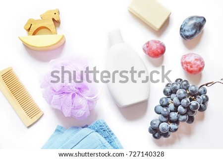 Beauty items. Bath accessories. Wooden comb, toy horse, purple sponge puff, blue terry towel, shampoo bottle, soap, plums and grapes. Flat lay bathroom items, top view stock photo