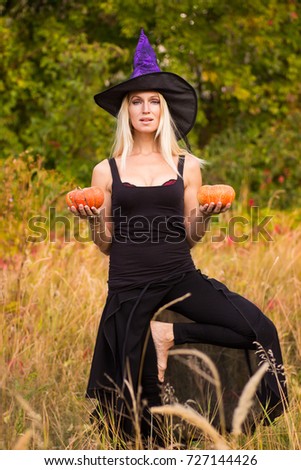 Happy female in Halloween witch costume practicing yoga positions with pumpkins in her hands