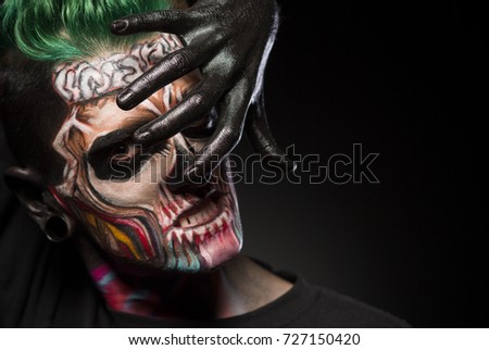 Bight makeup for Halloween party. Mans face with colored skull makeup, covering face with hand painted in black.