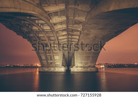 View under Vogresovsky Bridge through Voronezh river at night, dark toned cityscape