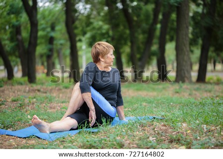 Senior lady doing yoga on a garden background. Hard yoga training. Yoga practice concept. Copy space.