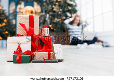 Winter holidays background. Christmas gift boxes band with red ribbons closeup at decorated xmas tree and happy young girl backdrop. Selective focus, copy space