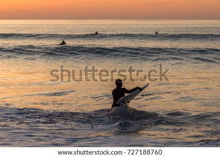 Surfer carrying the surfboard into water with waves in the sunset