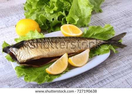 Smoked mackerele and lemon on green lettuce leaves on Wooden cutting board isolated on white background.