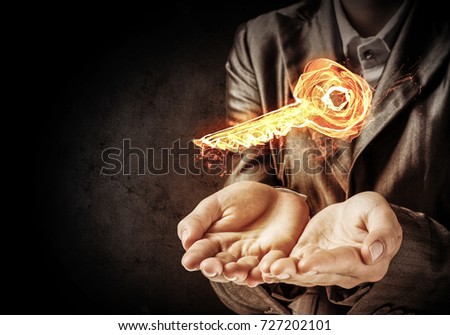 Closeup of businessman in black suit keeping flaming key symbol in hands with dark wall on background.
