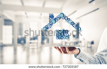 Close of businessman holding tablet pc with house sign made of connected gears. Mixed media