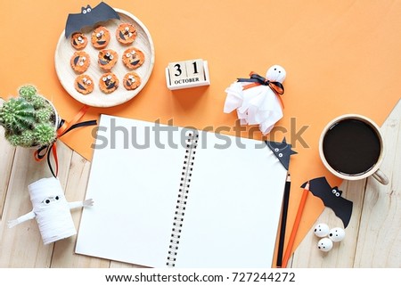 Halloween, celebration or holiday background concept : Mock up of open notebook, paper crafts, cube calendar, grilled carrots with scary face and coffee cup, Top view or flat lay with copy space