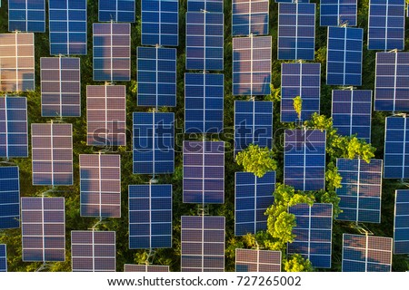 Top view of solar panels (solar cell) in solar farm with green tree and sun lighting reflect .Photovoltaic plant field. Royalty-Free Stock Photo #727265002