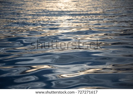 close up picture shows ripple of blue water with yellow light of sunset
