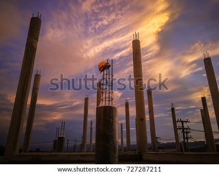 Silhouette image of building under construction in the sunset sky with helmet over the pole.This picture is have grain and blurred.