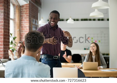 African american office worker dancing surrounded by colleagues. Happy entrepreneur performing victory dance, celebrating great achievement at work. Team of coworkers cheering him by clapping hands. 