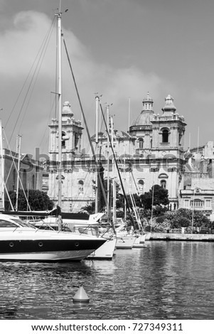 Yachts docked at the port of Malta. Boats moored in a row on the background of cathedral. Black and white picture