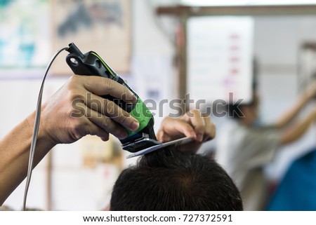 Close-up of a Thai man with a barber using clippers with black hair comb in a shop.