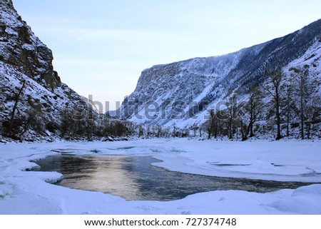 Snow-capped mountain ridge, river valley and partially frozen Chulyshman river in a clear evening in winter against the background of a bright blue sunset sky. Ulagan region, Altay, Russia.
