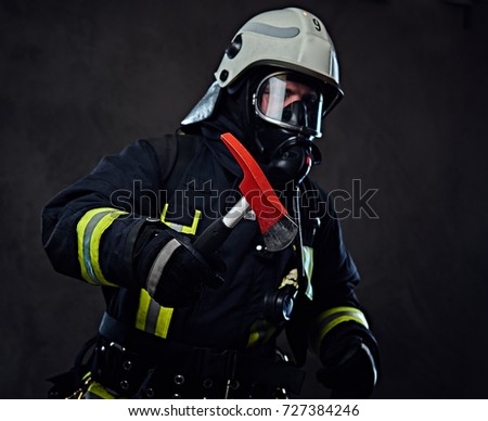 Firefighter dressed in a uniform and an oxygen mask holds a red axe.