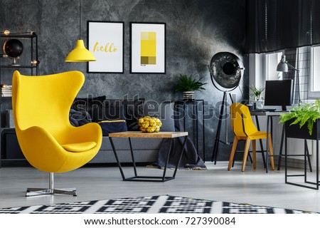 Designer's yellow chair next to simple table in living room with work area next to the window