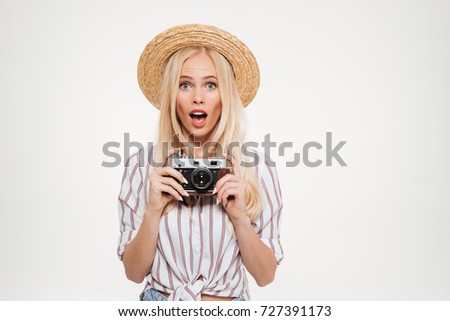 Portrait of pretty excited woman in hat holding a camera isolated over white background