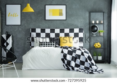 Black and white checkered bedsheets and yellow pillow on bed in bedroom with metal shelf