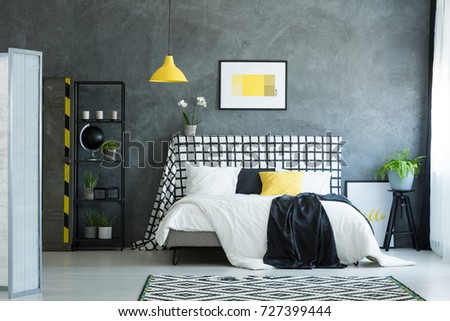 Black and white bedsheets on king-size bed against dark textured wall in bedroom with plant in blue pot on black stool