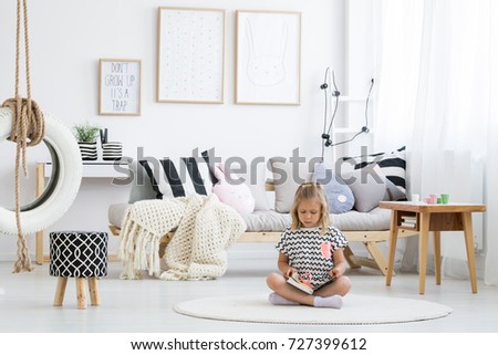 Girl in striped shirt reads book on white round carpet in kid room with tire on line