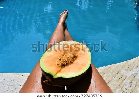 Summer healthy breakfast near pool. Melon on a lap and legs in water. Fruits and body. Summer vacation. 