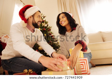 Smiling man helping his wife put presents under Christmas tree