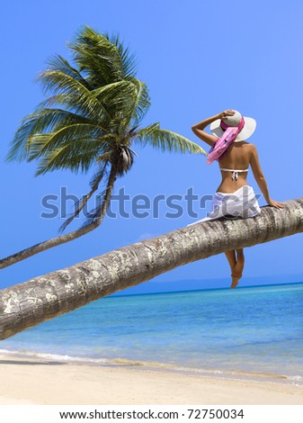 Woman on the beach sitting back on palm tree
