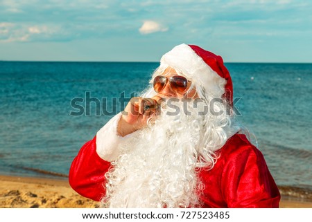 Santa Claus on the beach sits in a chair and smokes a cigar.