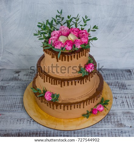 a three-tiered wedding chocolate drip cake decorated with roses