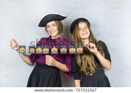 Portrait of two happy young women in black witch halloween costumes over gray background. The concept of Halloween, funny faces. Teenage girls with pictures of pumpkins with different emotions. 
