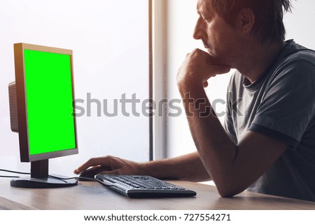 Freelancer working on home office desktop PC computer. Monitor has green screen as mock up copy space.