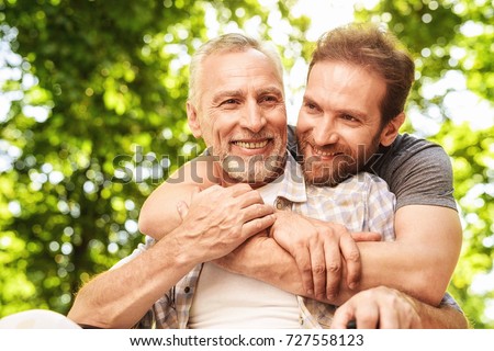 The old man on a wheelchair and his son are walking in the park. A man hugs his elderly father. They are happy and smiling Royalty-Free Stock Photo #727558123
